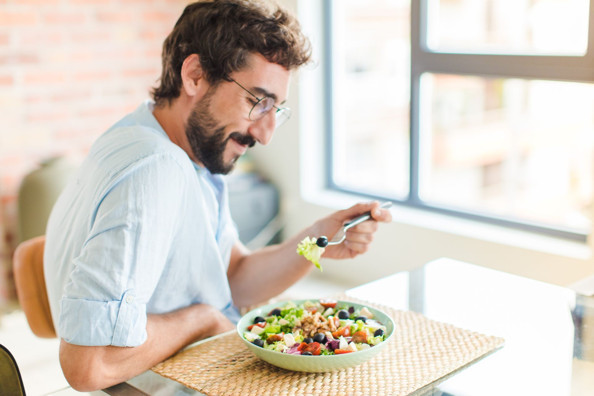 Man eating a salad at a bright table by a window
