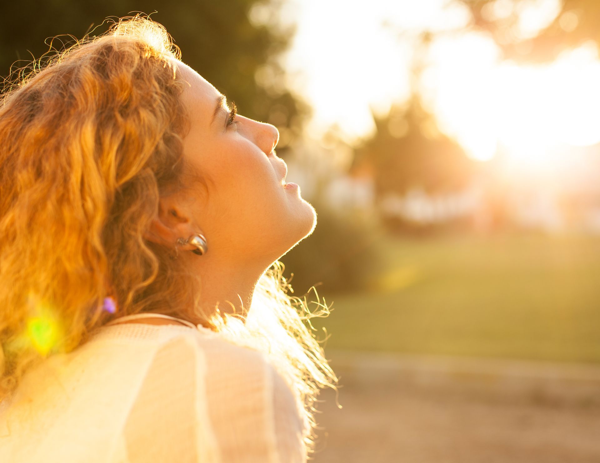 Person in a sunlit field looking up with eyes closed, backlit by warm golden sunlight