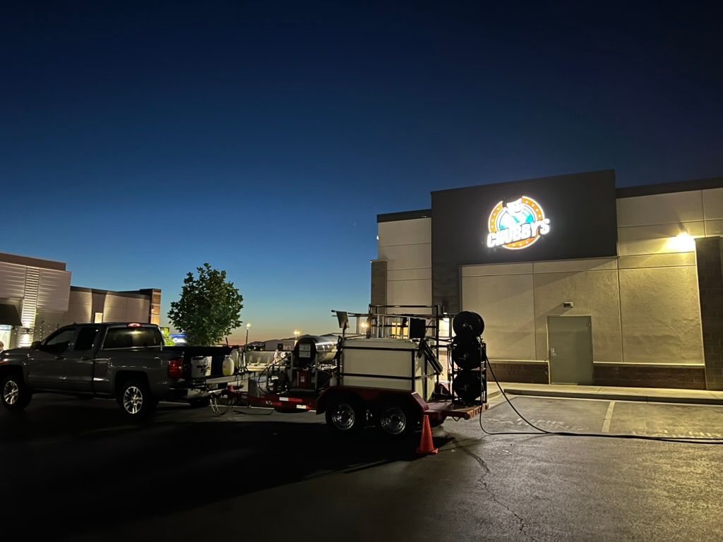Pickup truck and pressure washing equipment parked outside a brightly lit commercial building at dusk. A logo is visible on the building.