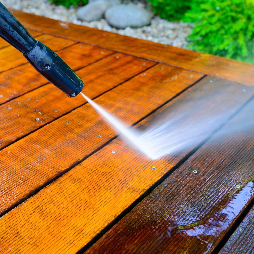 A person operates a pressure washer to clean a wooden deck, showcasing the cleaning process for outdoor maintenance.