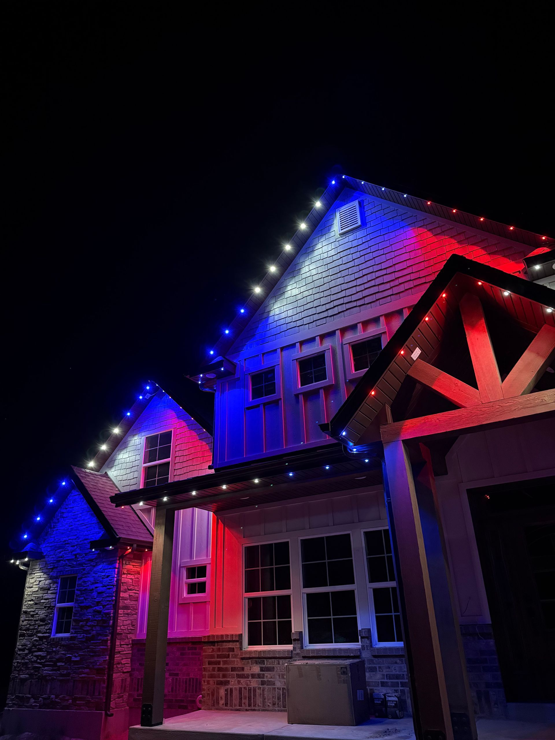 A house with steep roofs is adorned with bright red, white, and blue lights against a dark night sky, creating a festive and vibrant atmosphere.