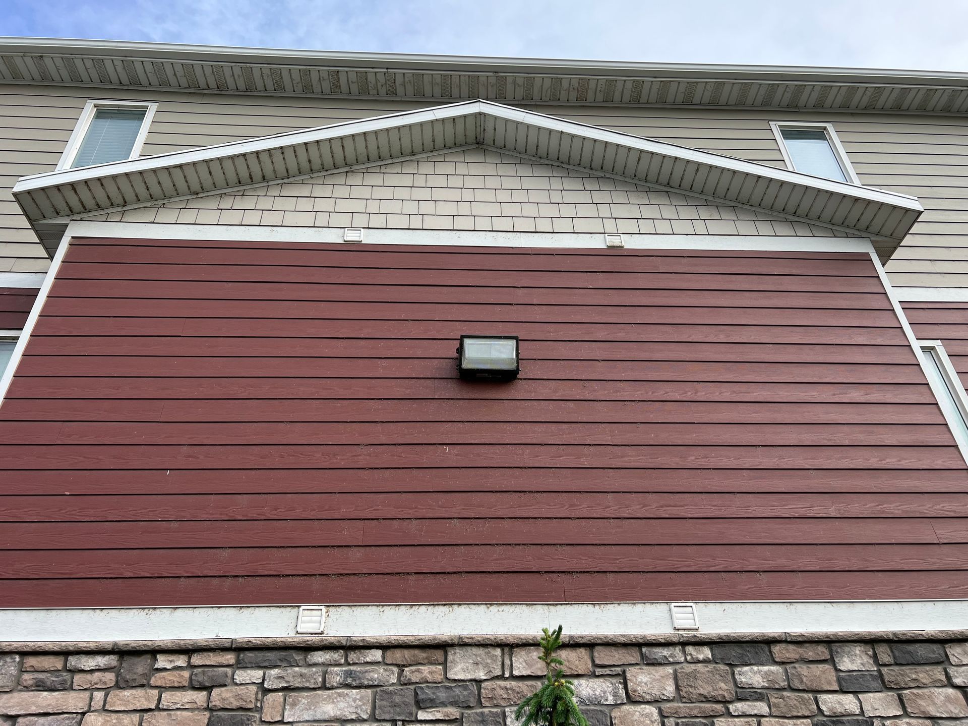 The image shows the exterior of a building with distorted red siding beneath a stone foundation. A wall light fixture is centered on the red section, creating an unusual visual effect.