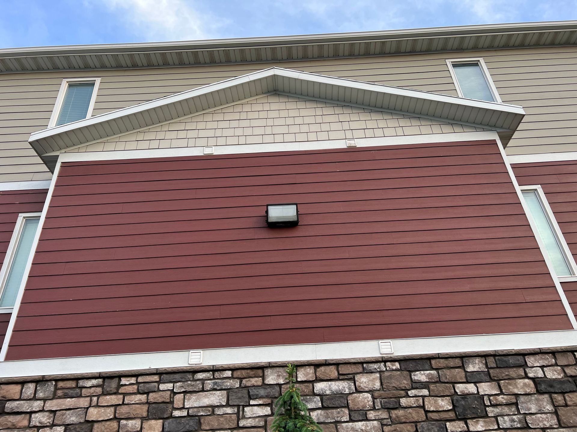 A building's exterior with red and beige siding shows noticeable wind damage, creating a wavy texture. A single light fixture is centered on the red section.