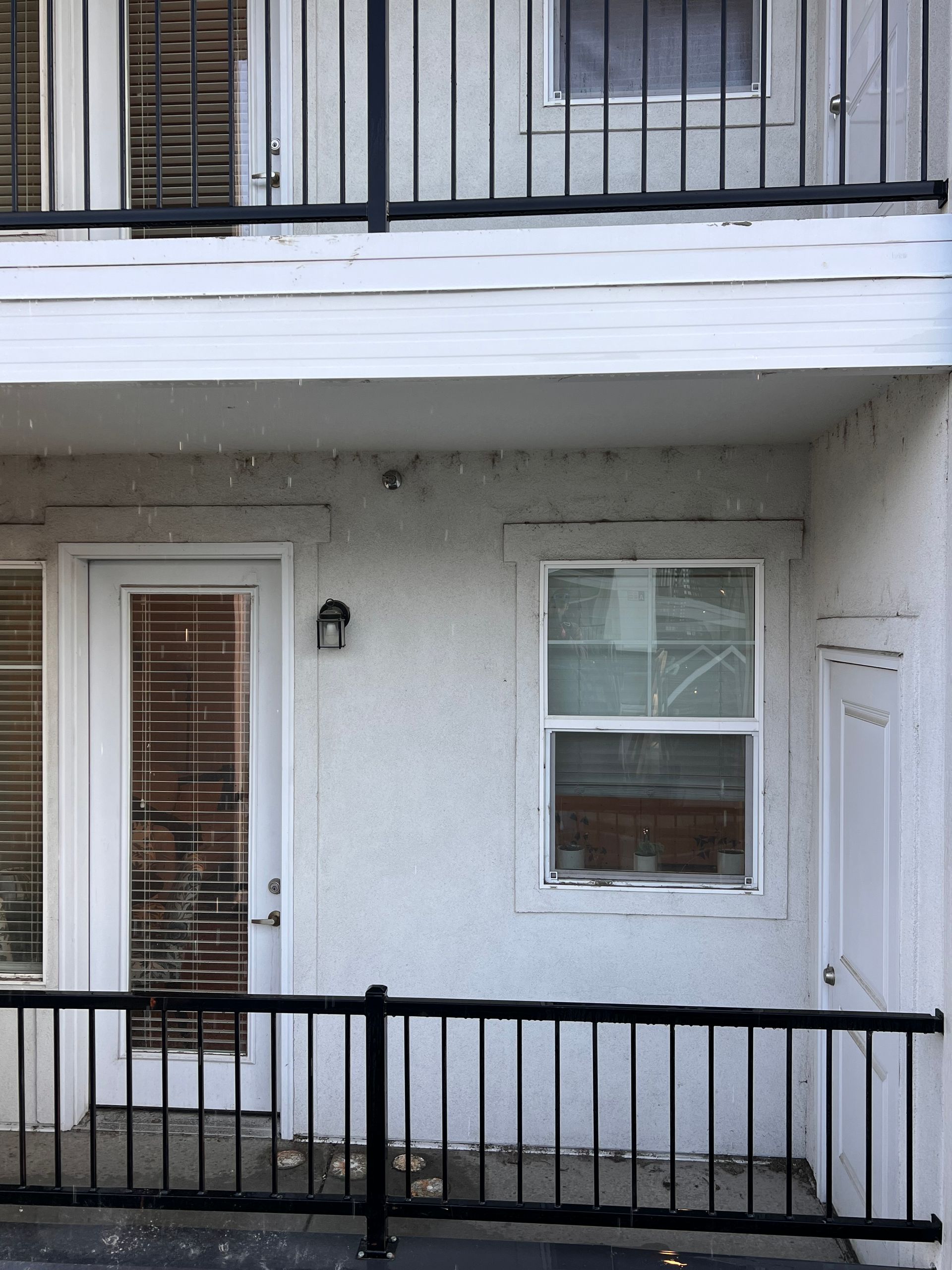 A gray exterior wall features a glass door with blinds, a window, and a light fixture. Snow falls gently, creating a tranquil winter atmosphere.