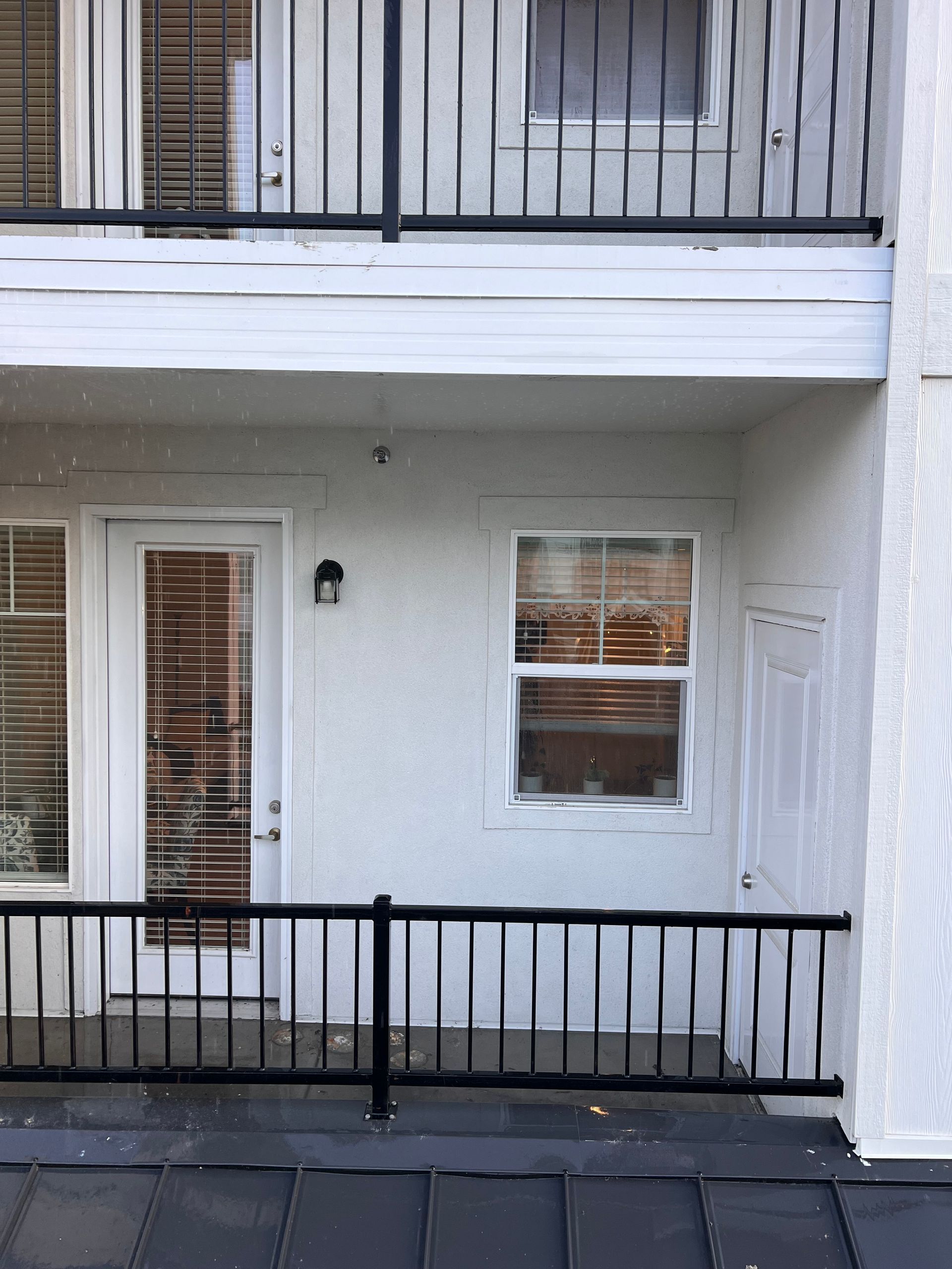 Exterior of a house showing a snow-covered upper wall, a glass door with blinds, a window, and a simple light fixture, creating a calm, wintry scene.