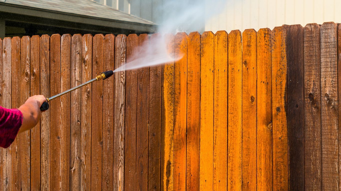 A person uses a hose to spray a fence, part of the Satisfy Utah project aimed at enhancing local environments.