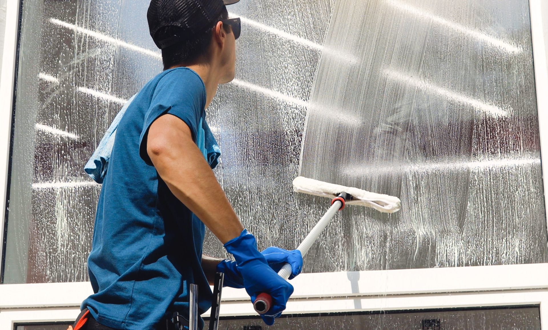 A man wearing a blue shirt and gloves is cleaning a window as part of the Satisfy Utah campaign.