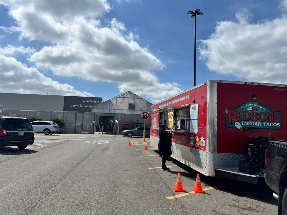 A food truck is parked in a parking lot in front of a building.
