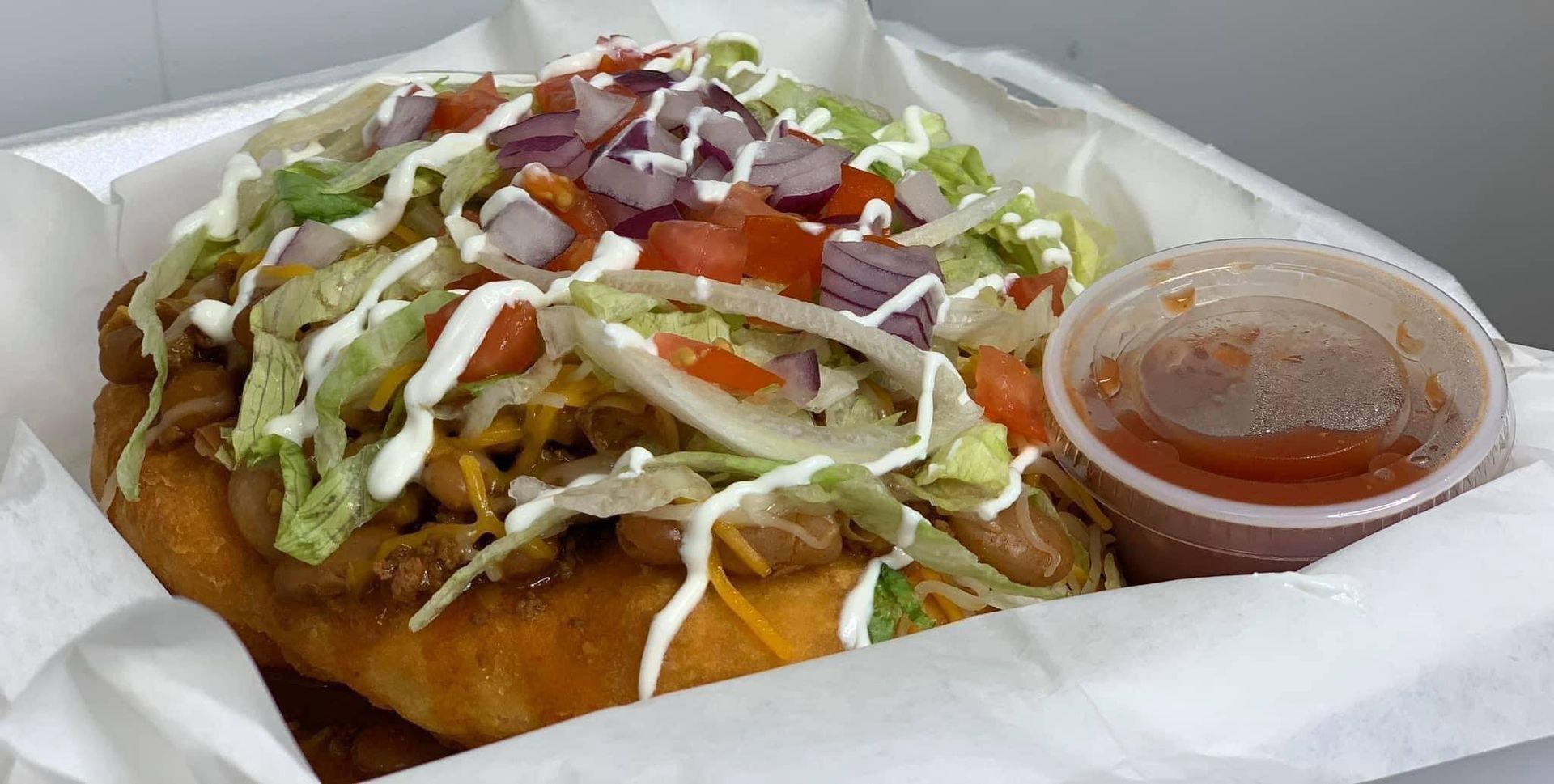 A close up of a taco in a styrofoam container with a cup of sauce.
