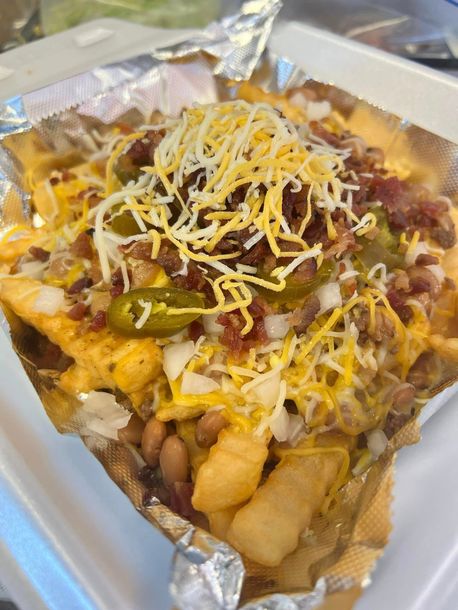 A close up of a plate of food with french fries , cheese , beans and bacon.