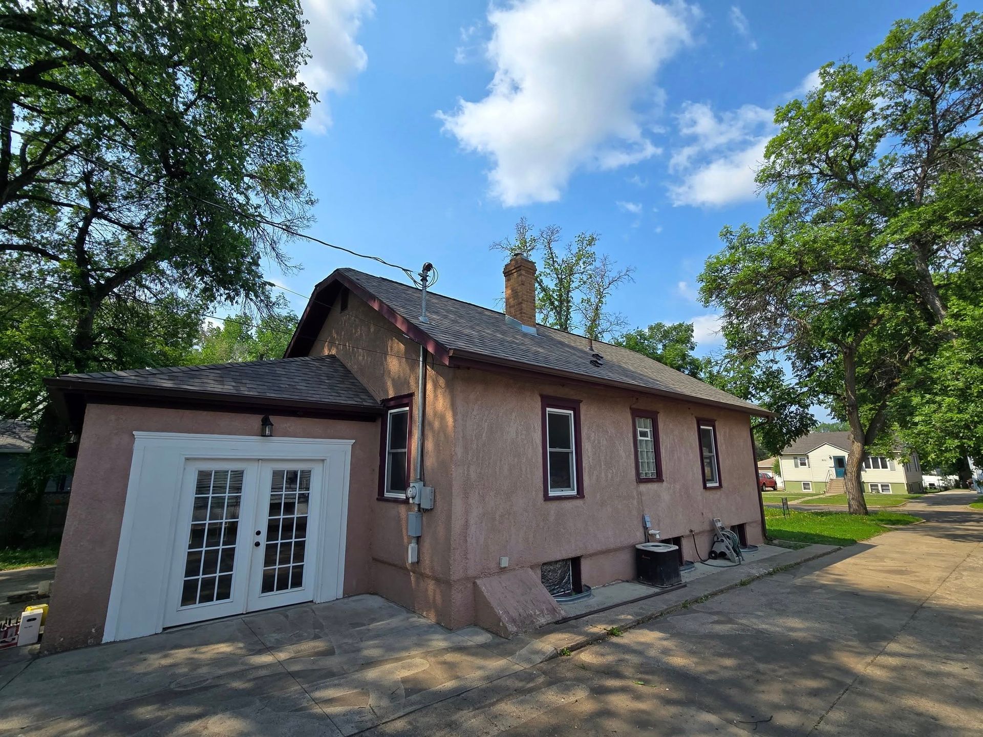 Pink stucco building with white double doors, windows, and trees under a cloudy blue sky.