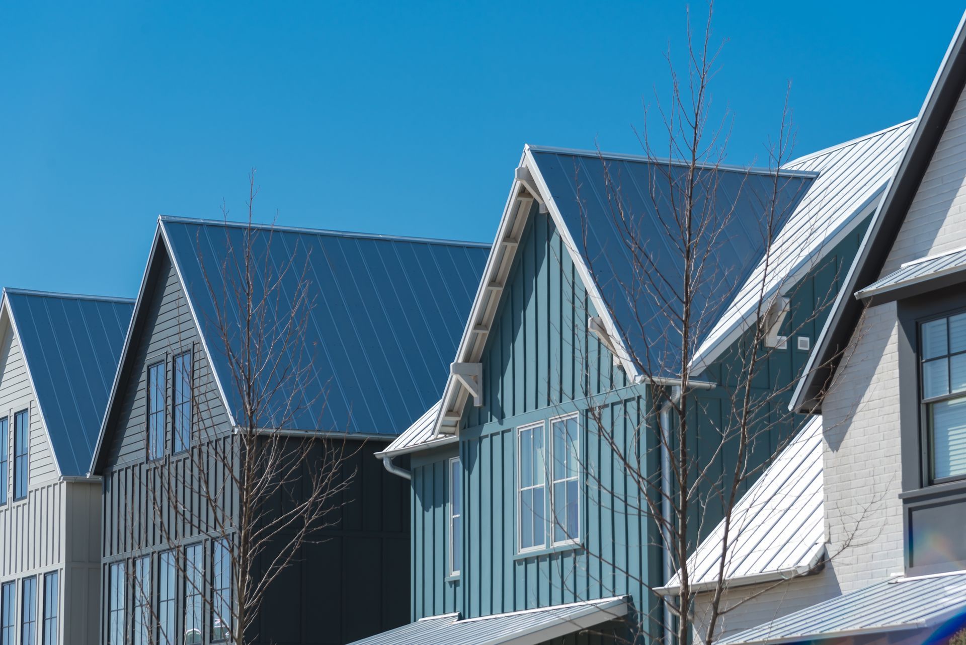Row of modern houses with blue, gray, and white siding, under a clear blue sky.