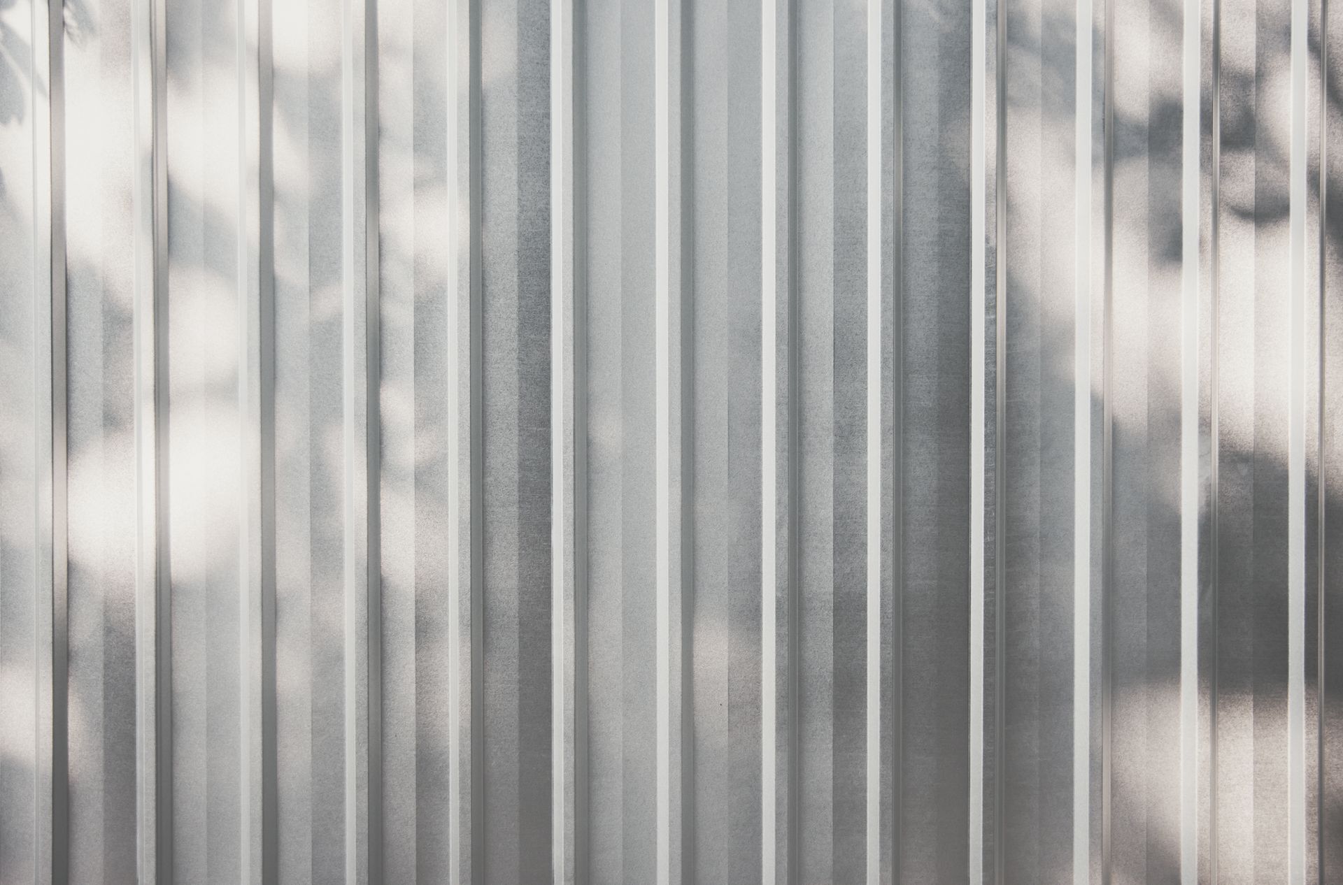 Corrugated metal fence with sunlight shadows.