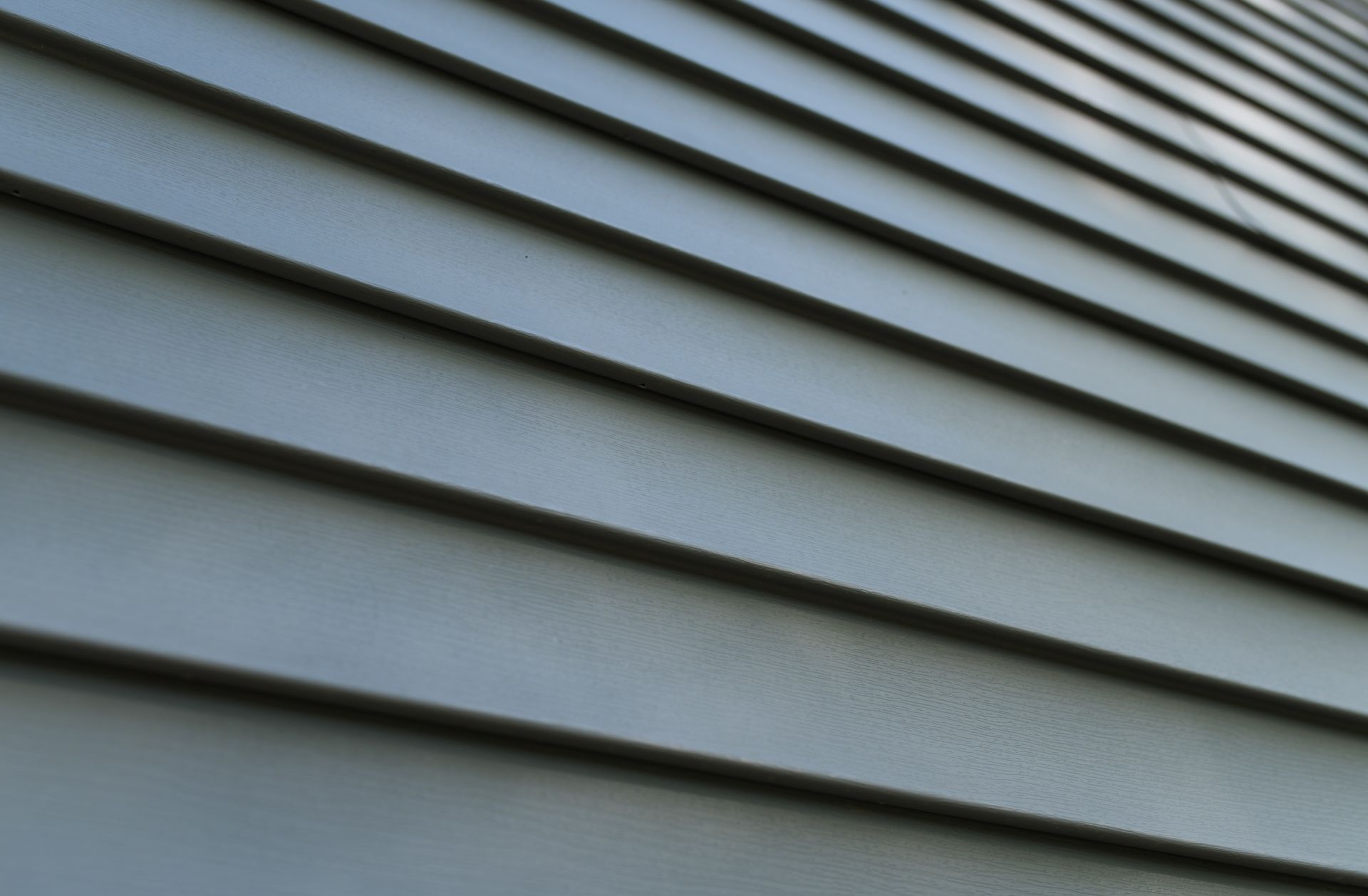 Close-up of gray horizontal siding on a building, angled, with shadows highlighting the texture.