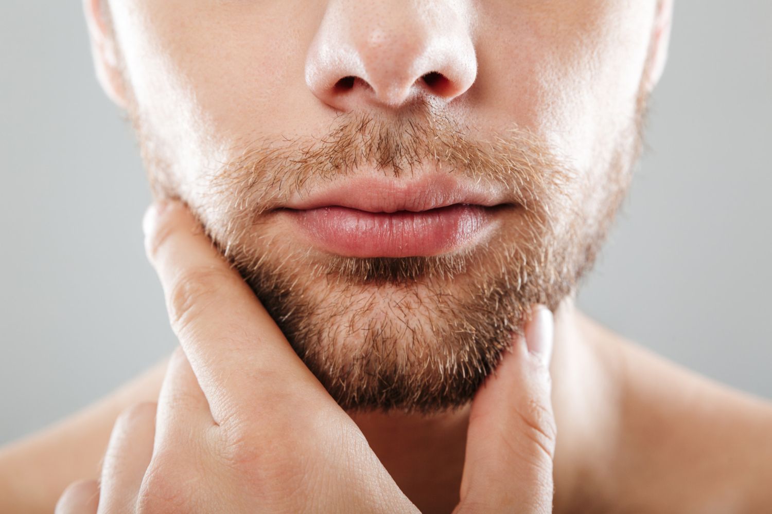 Close-up of a man touching his beard with his fingers, neutral expression.