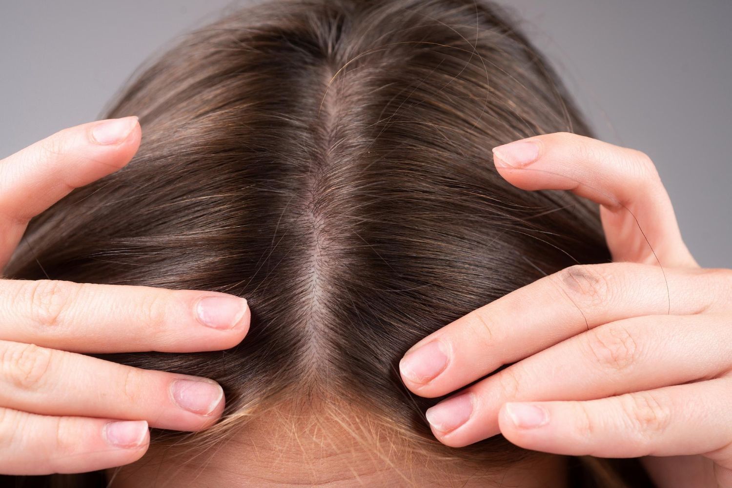 Person parting brown hair, fingers on either side of the part, close-up of scalp.