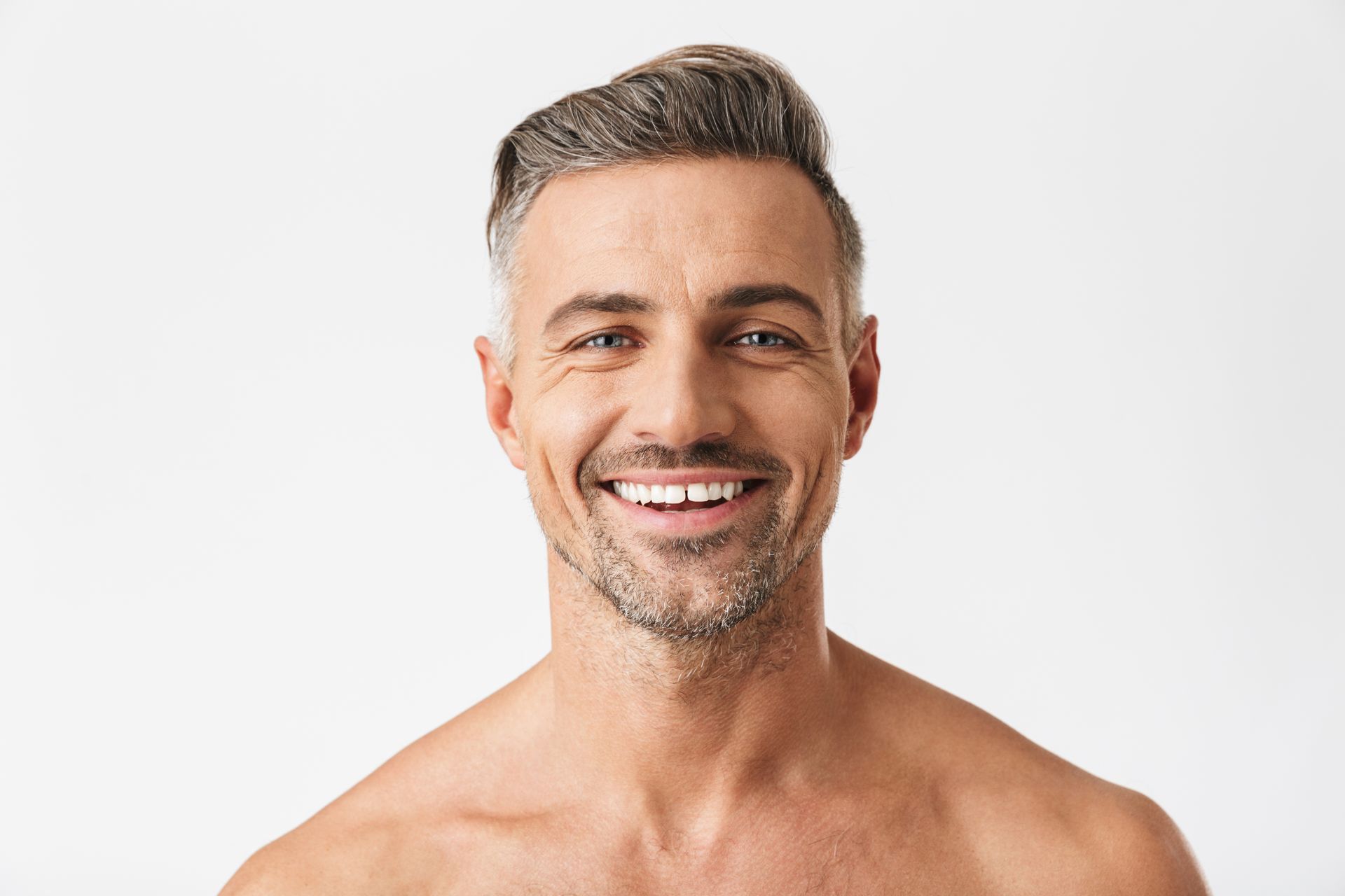 A shirtless man with a beard is smiling and looking at the camera over a white background.