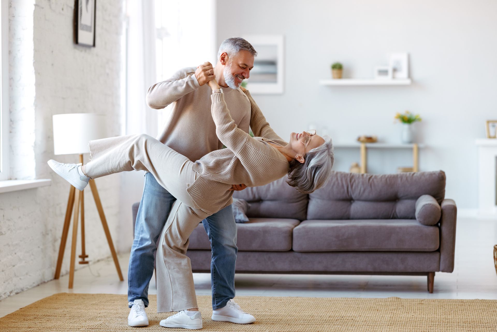 A man is holding an older woman in his arms in a living room.