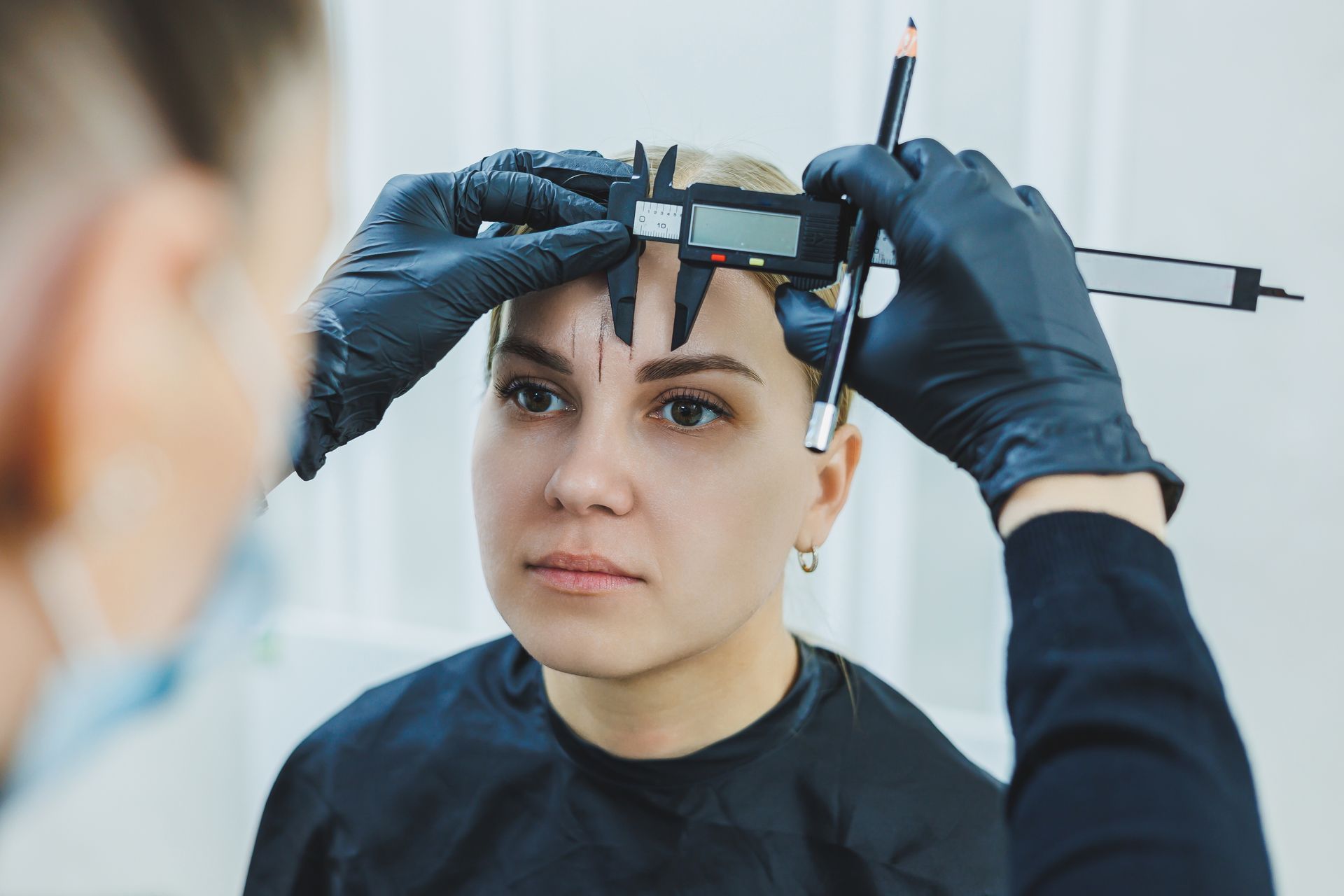 A woman is getting her eyebrows measured by a tattoo artist.