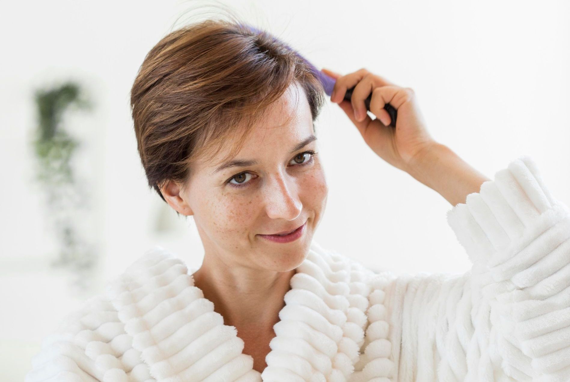 A woman in a white robe is brushing her hair.