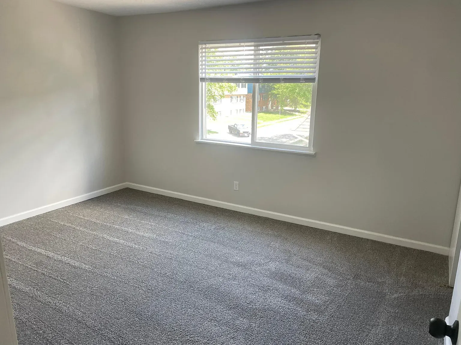 An empty bedroom with a large window and a carpeted floor.