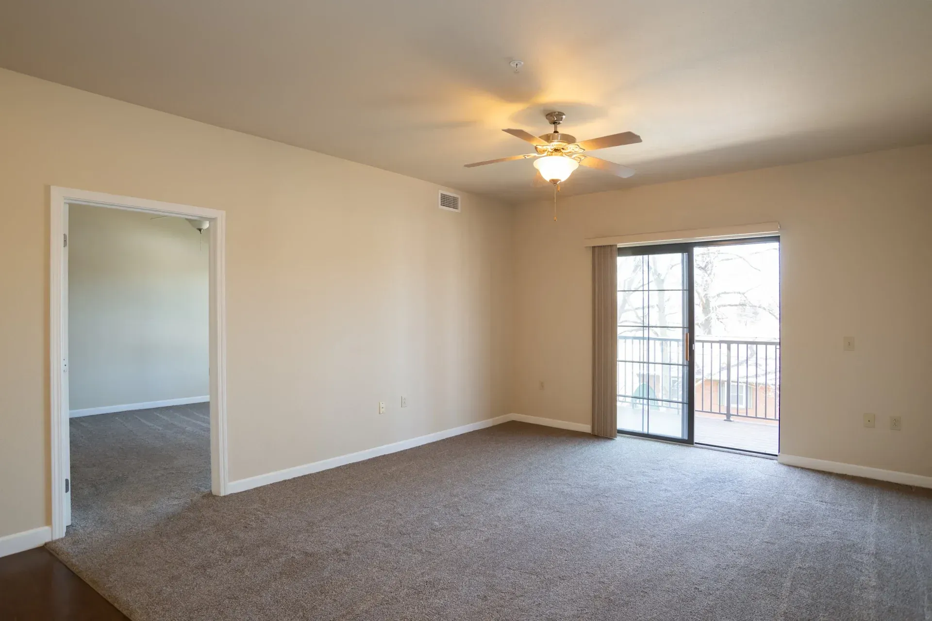 An empty living room with a ceiling fan and sliding glass doors.