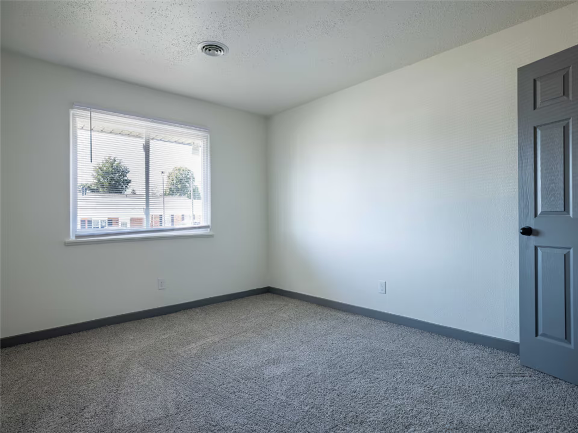 An empty bedroom with a window and a gray door.