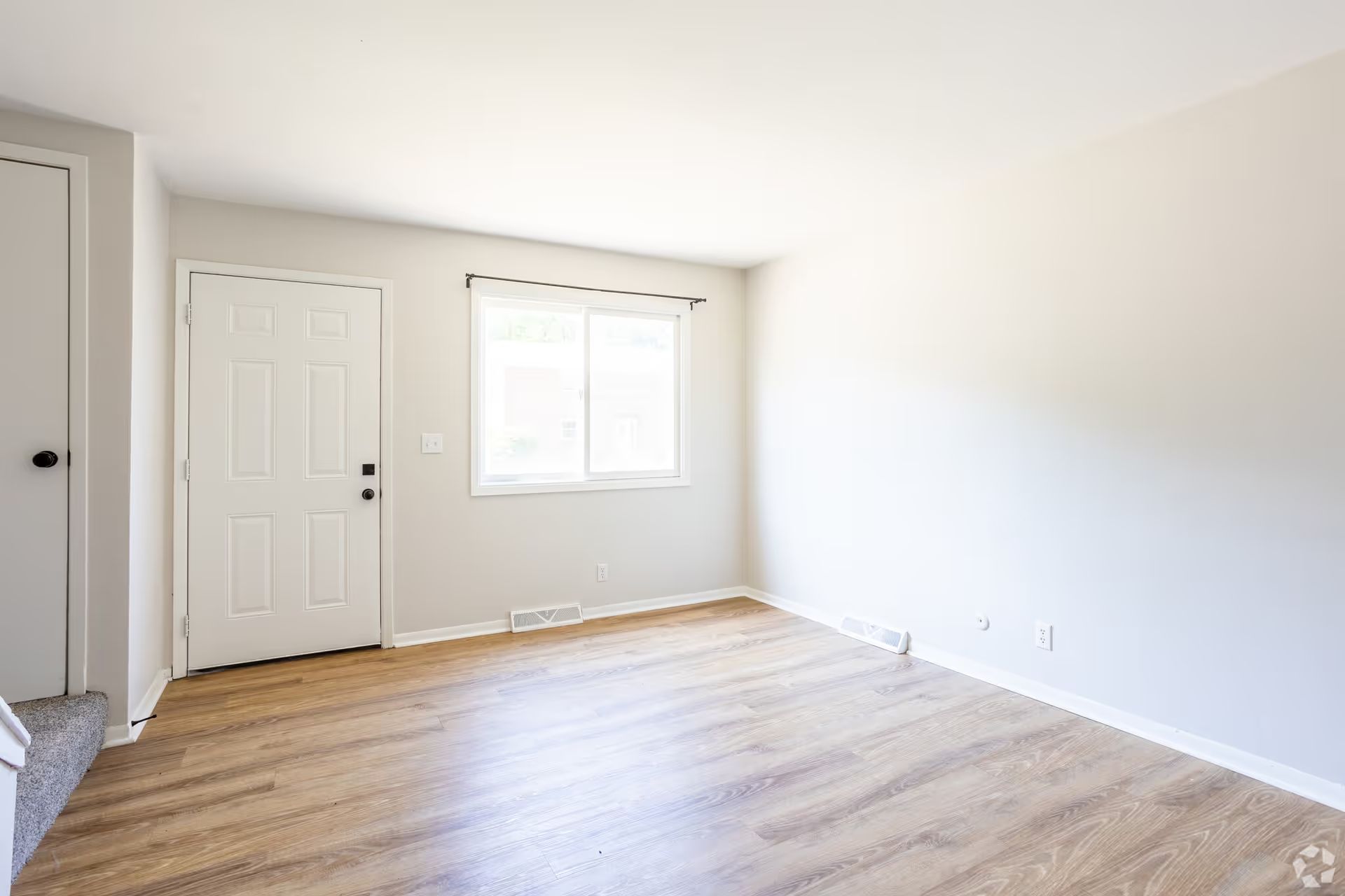 An empty living room with hardwood floors and a window.