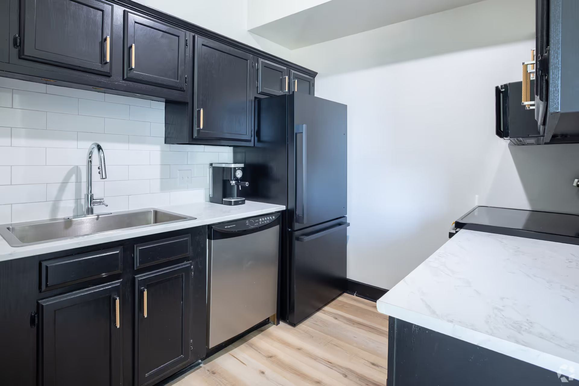 A kitchen with black cabinets , stainless steel appliances , a sink , and a refrigerator.