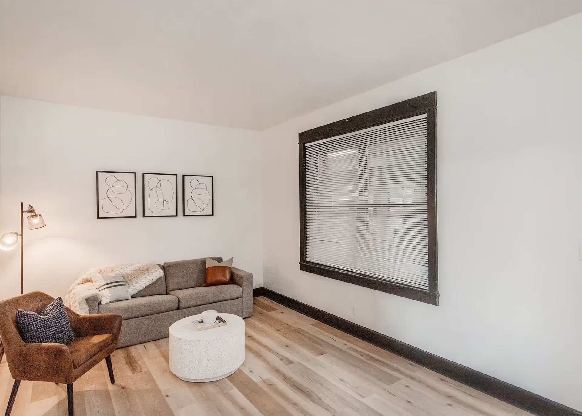 A living room with a couch , chair , coffee table and a large painting on the wall.