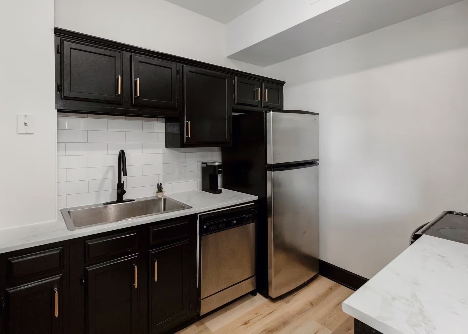 A kitchen with black cabinets , stainless steel appliances , a sink and a refrigerator.