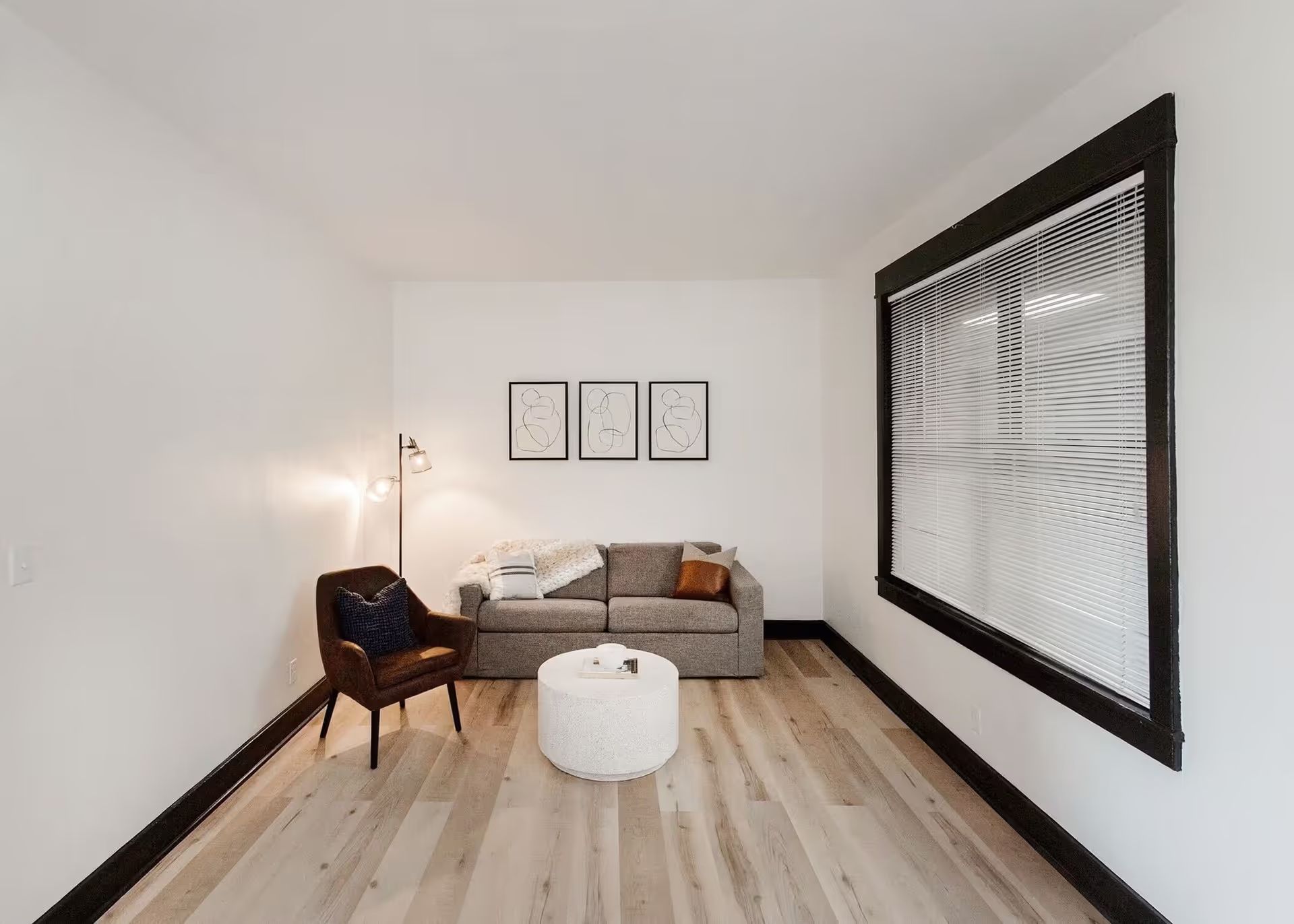A living room with a couch , chair , coffee table and two windows.