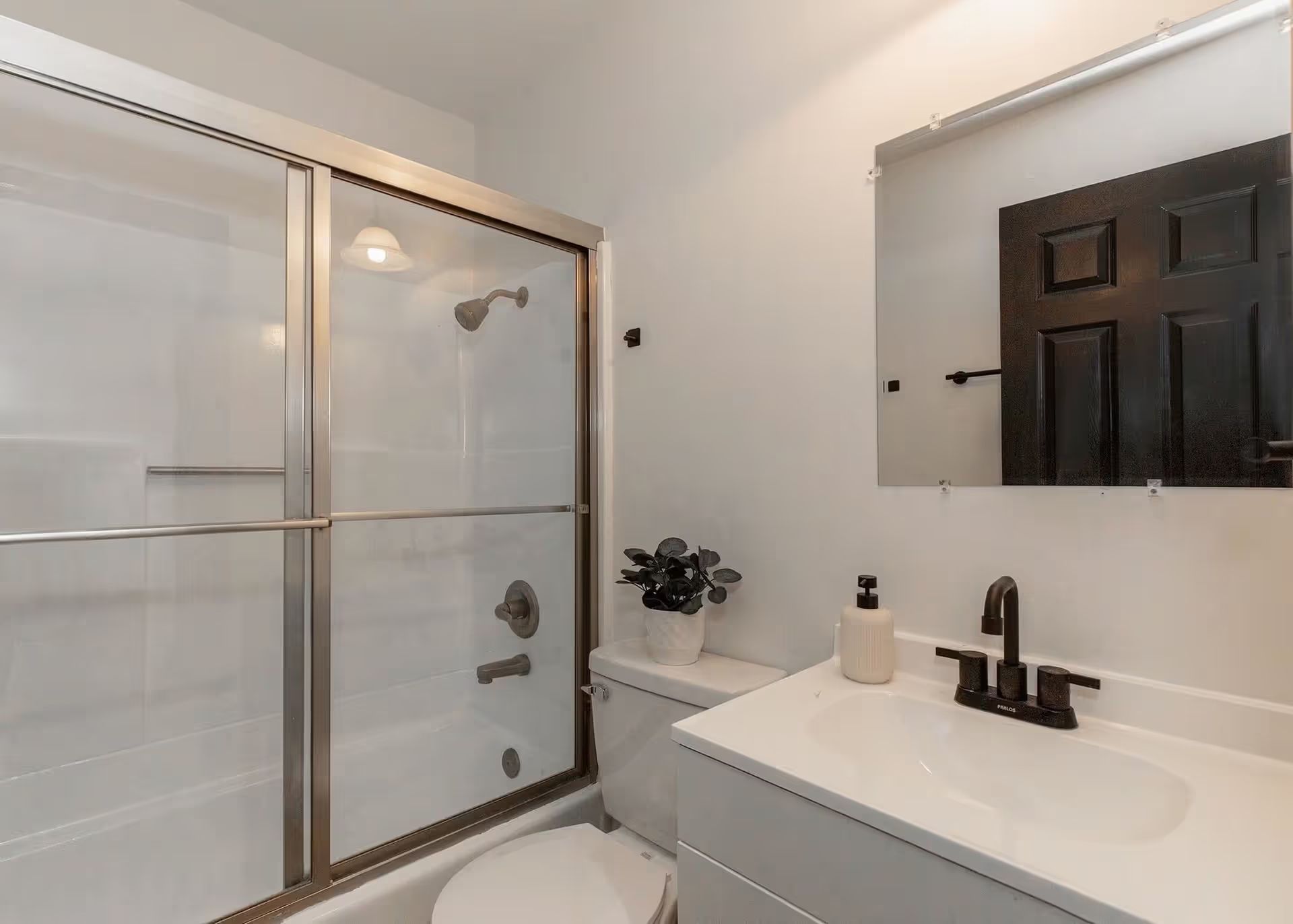 A bathroom with a toilet , sink , shower and mirror.