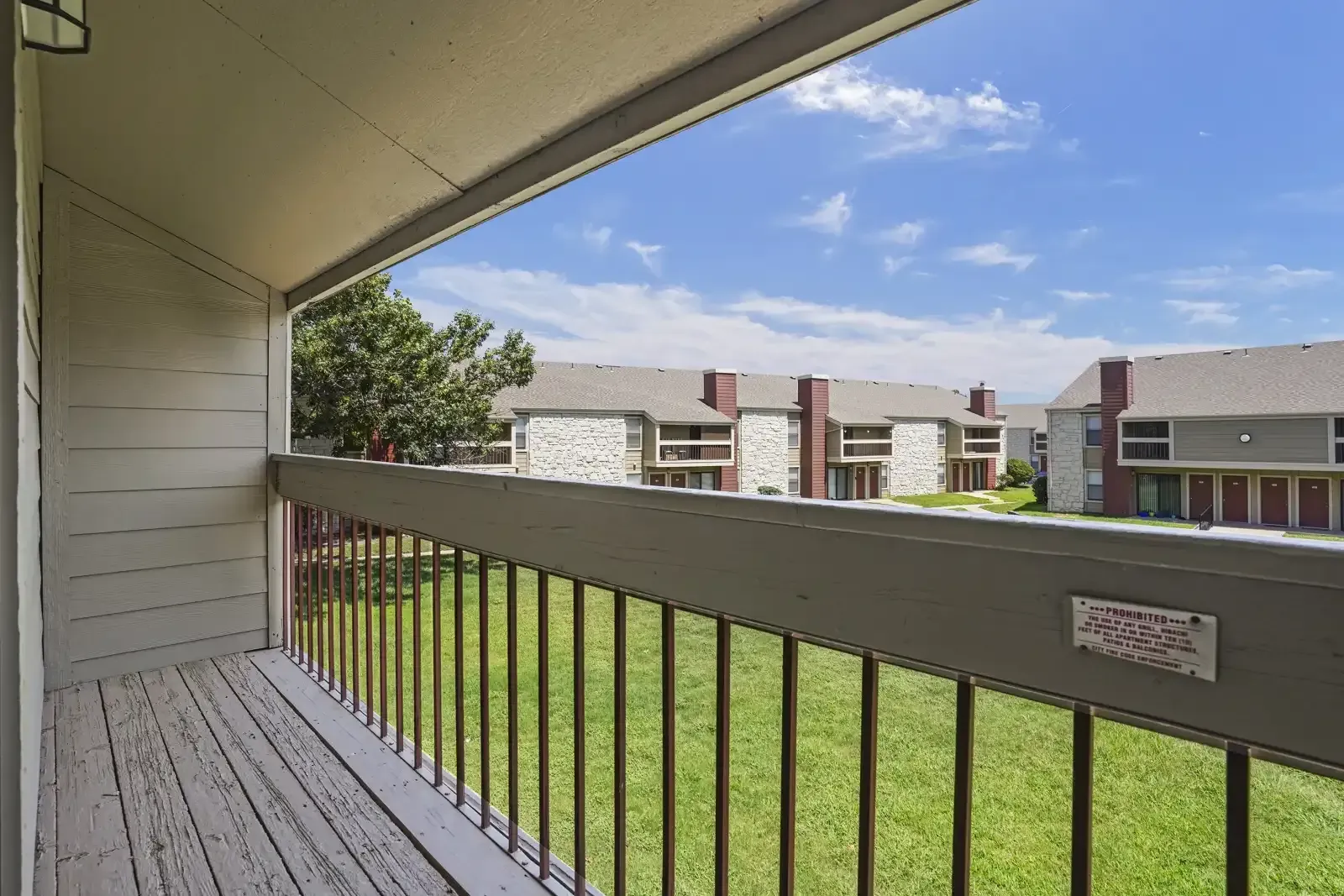 View from a balcony overlooking grassy area and nearby buildings.