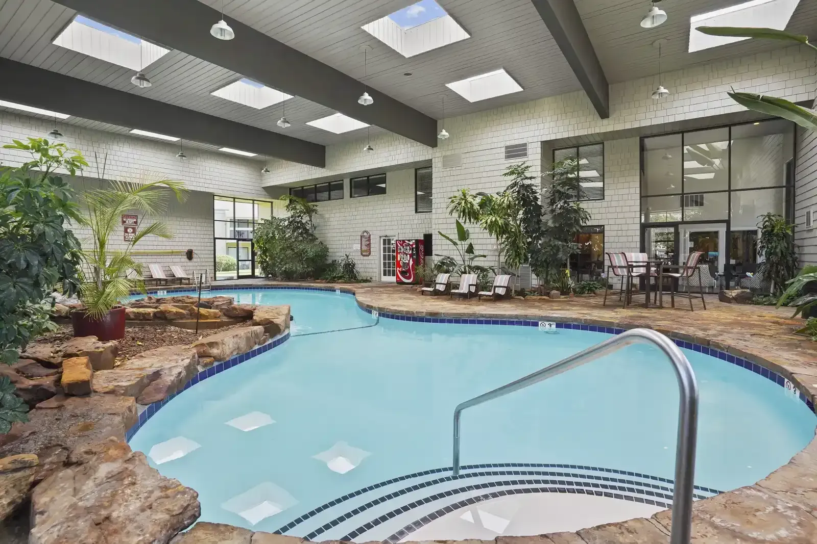 Indoor swimming pool surrounded by lush greenery and seating area.