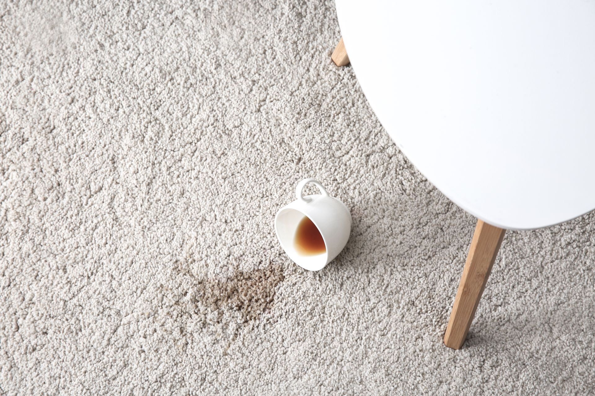 A cup of coffee spilled on a carpet next to a table.