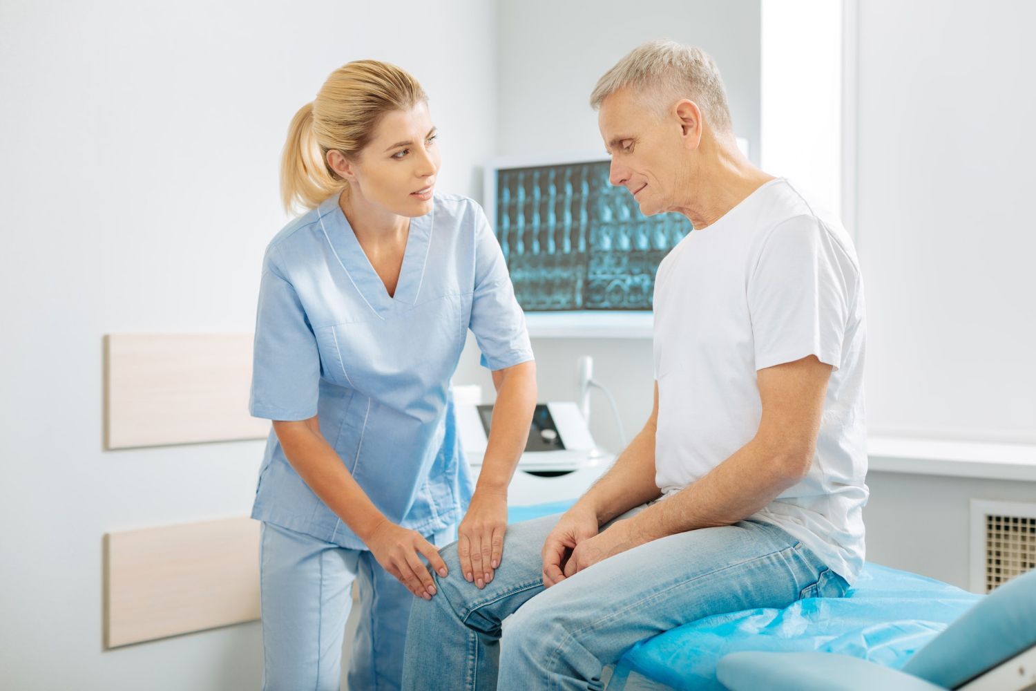 A healthcare worker examines a patient's knee in an exam room.