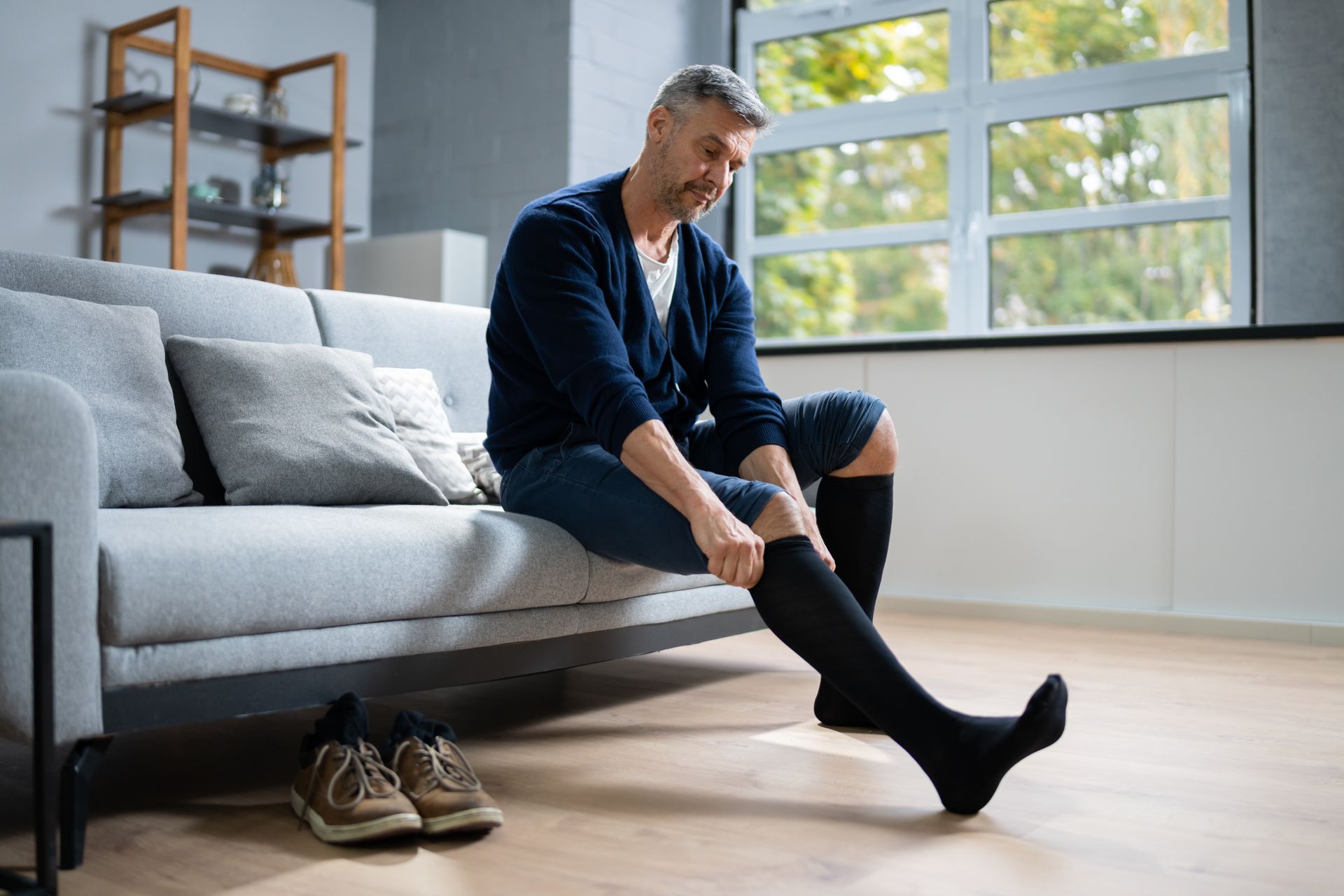 A man is sitting on a couch putting on compression socks.