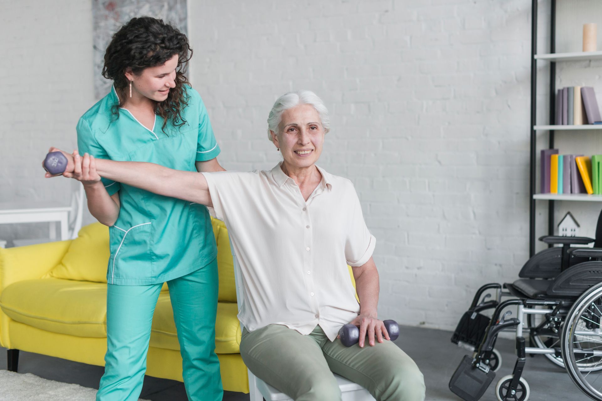 A nurse is helping an elderly woman in a wheelchair with a dumbbell.