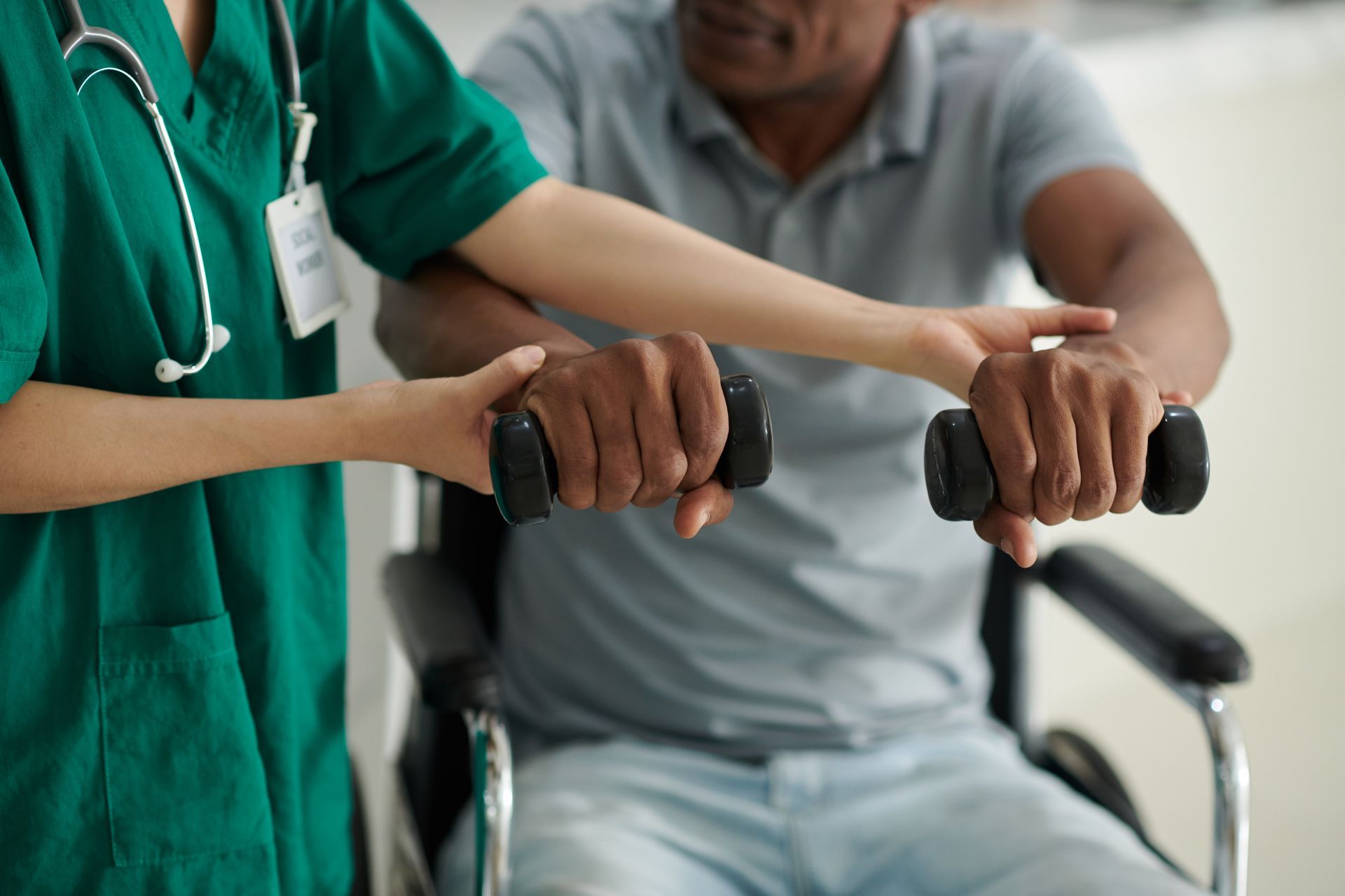 A nurse is helping a man in a wheelchair with dumbbells.