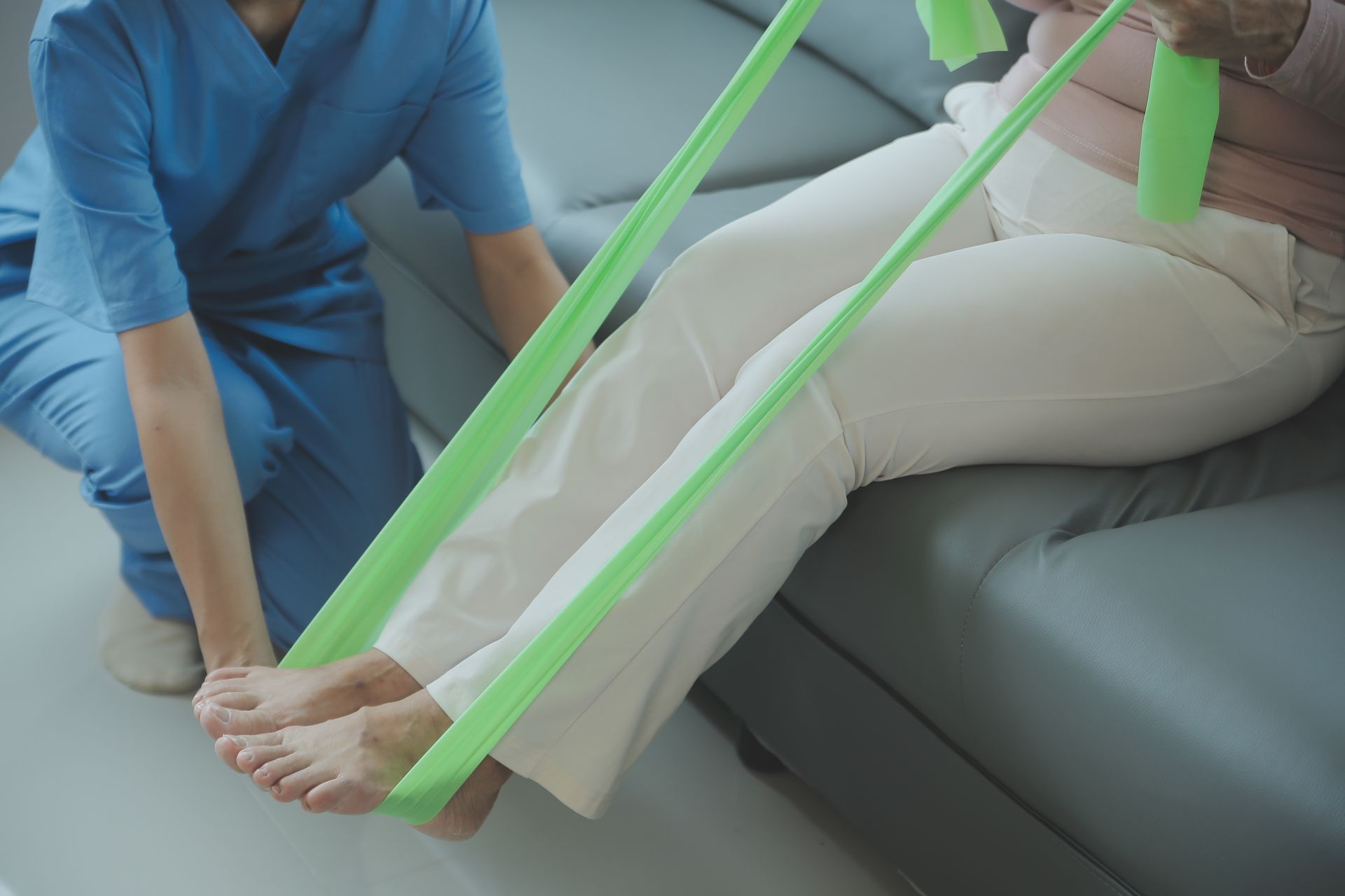 A nurse is helping an elderly woman stretch her legs with a resistance band.