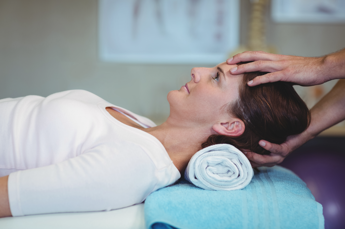 A woman is laying on a table getting a head massage.