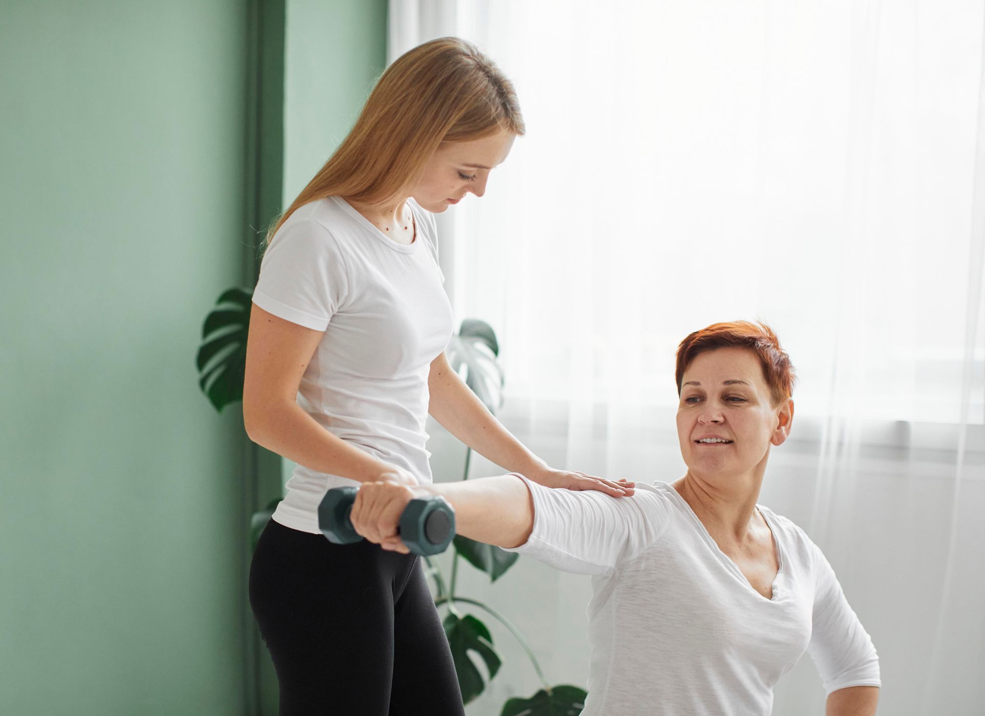 A woman is helping an older woman lift a dumbbell.