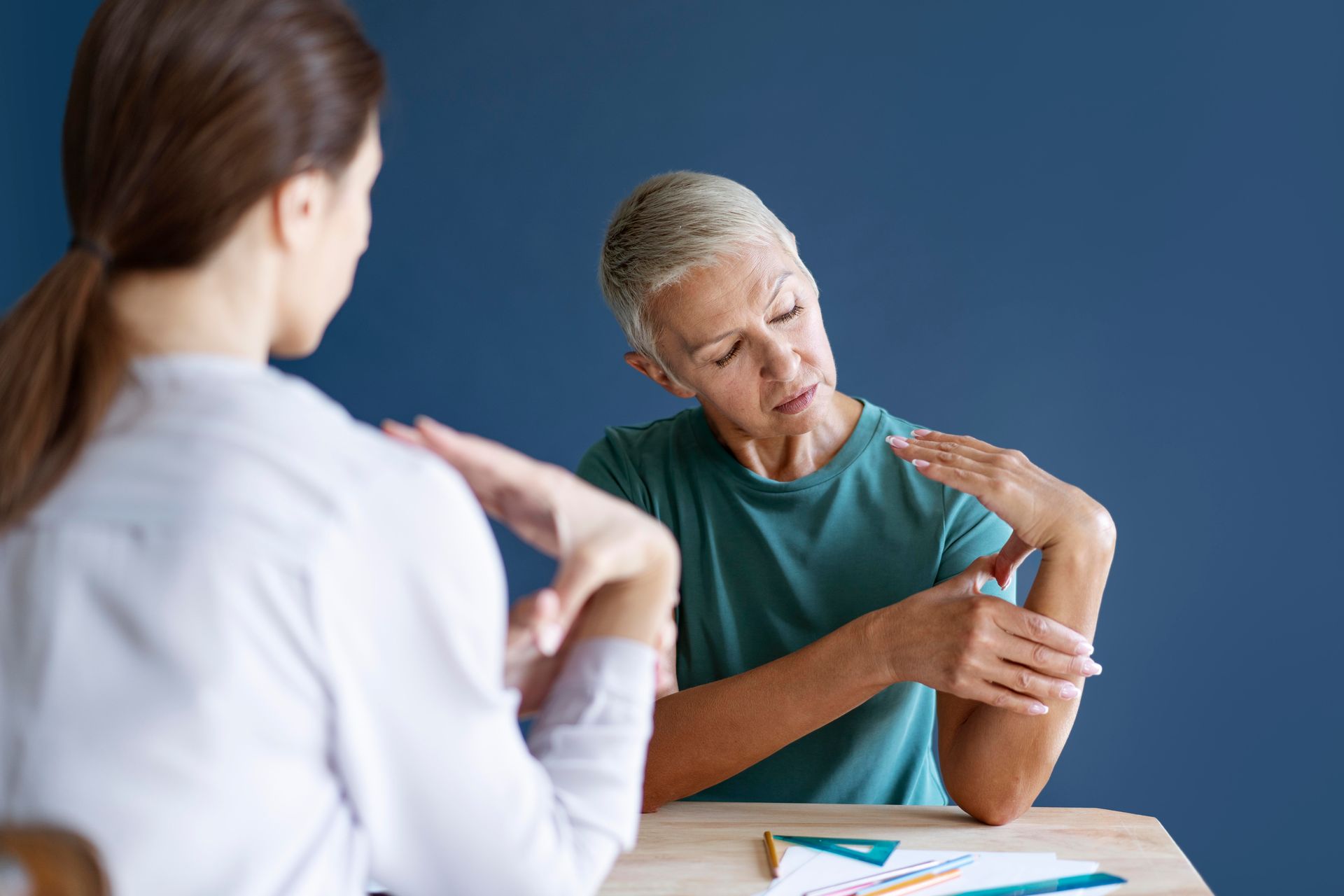 An elderly woman is sitting at a table talking to a doctor.