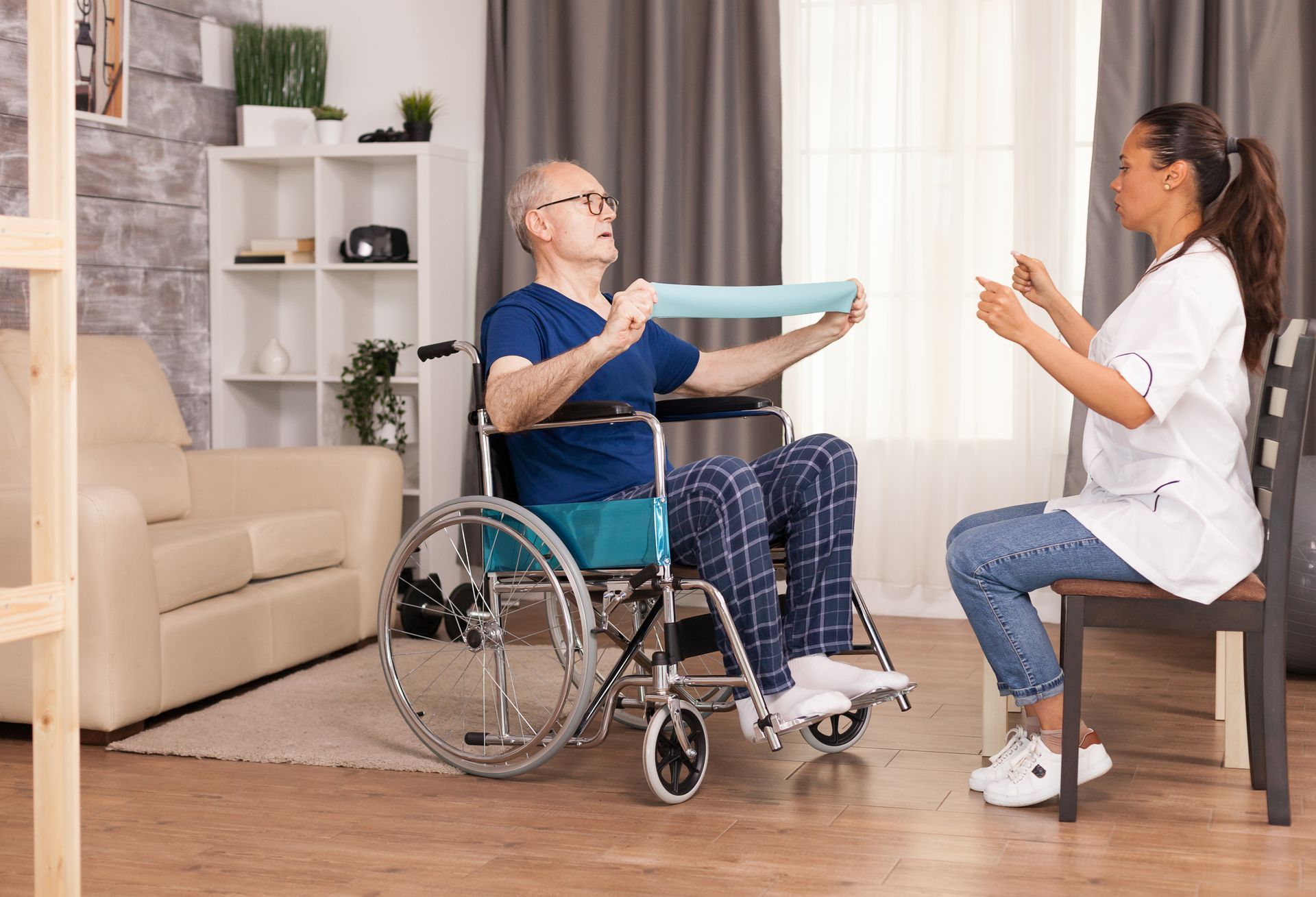 An elderly man in a wheelchair is doing exercises with a nurse.