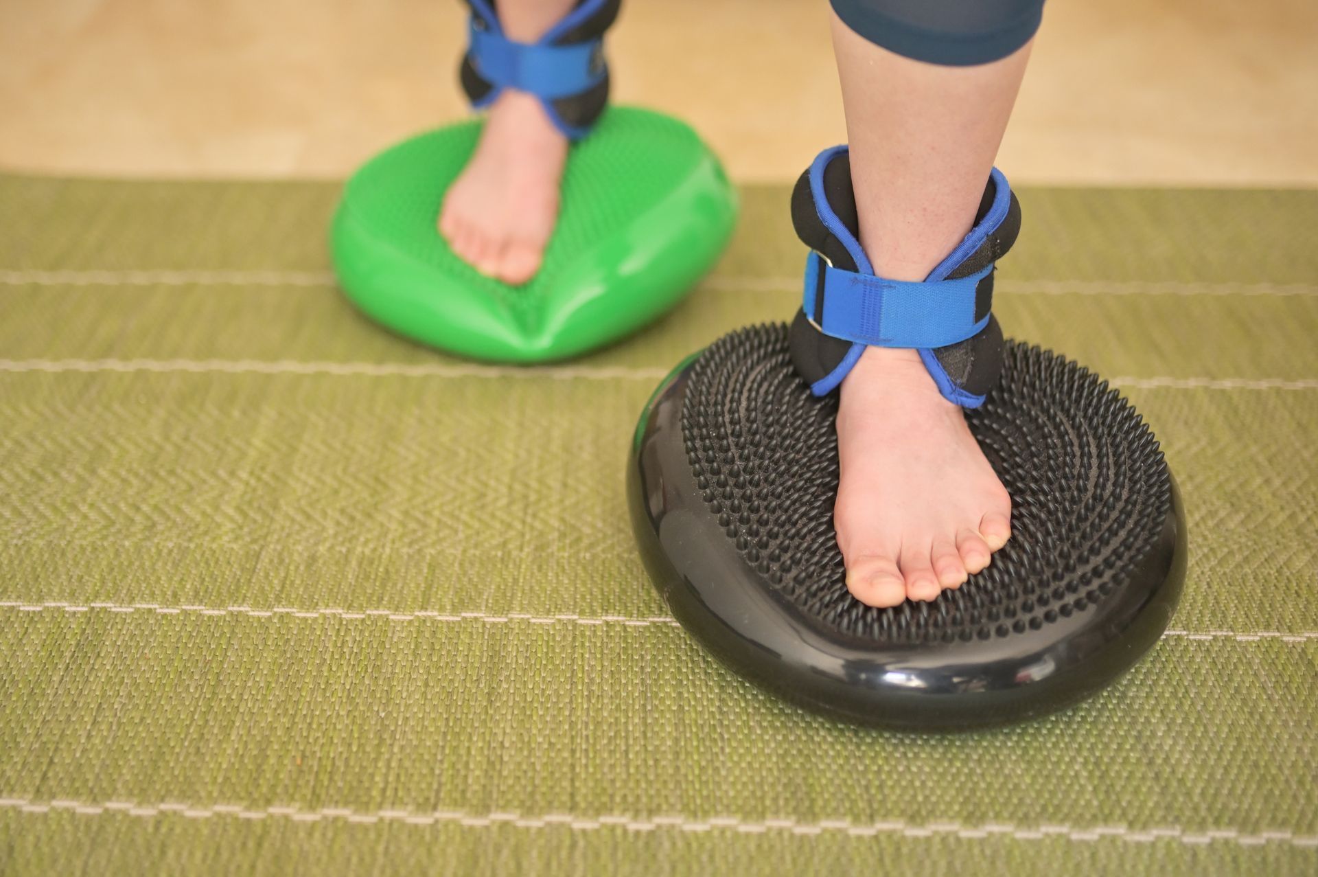 A person is standing on a balance cushion with weights on their ankles.