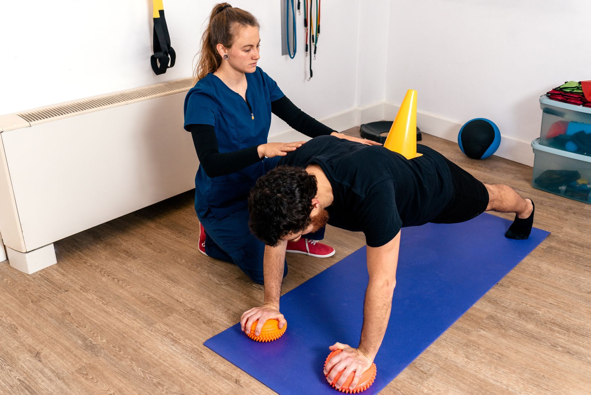 A woman is helping a man do push ups on a yoga mat.