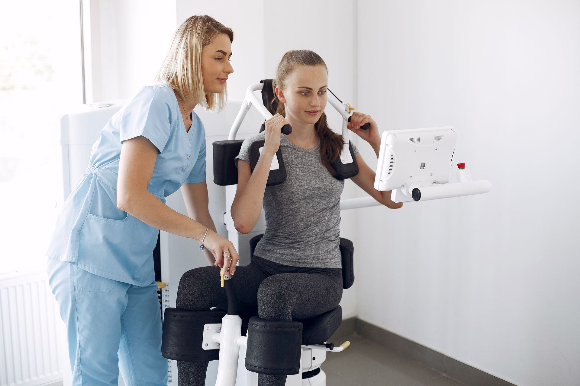 A woman is sitting on a machine with a nurse standing next to her.