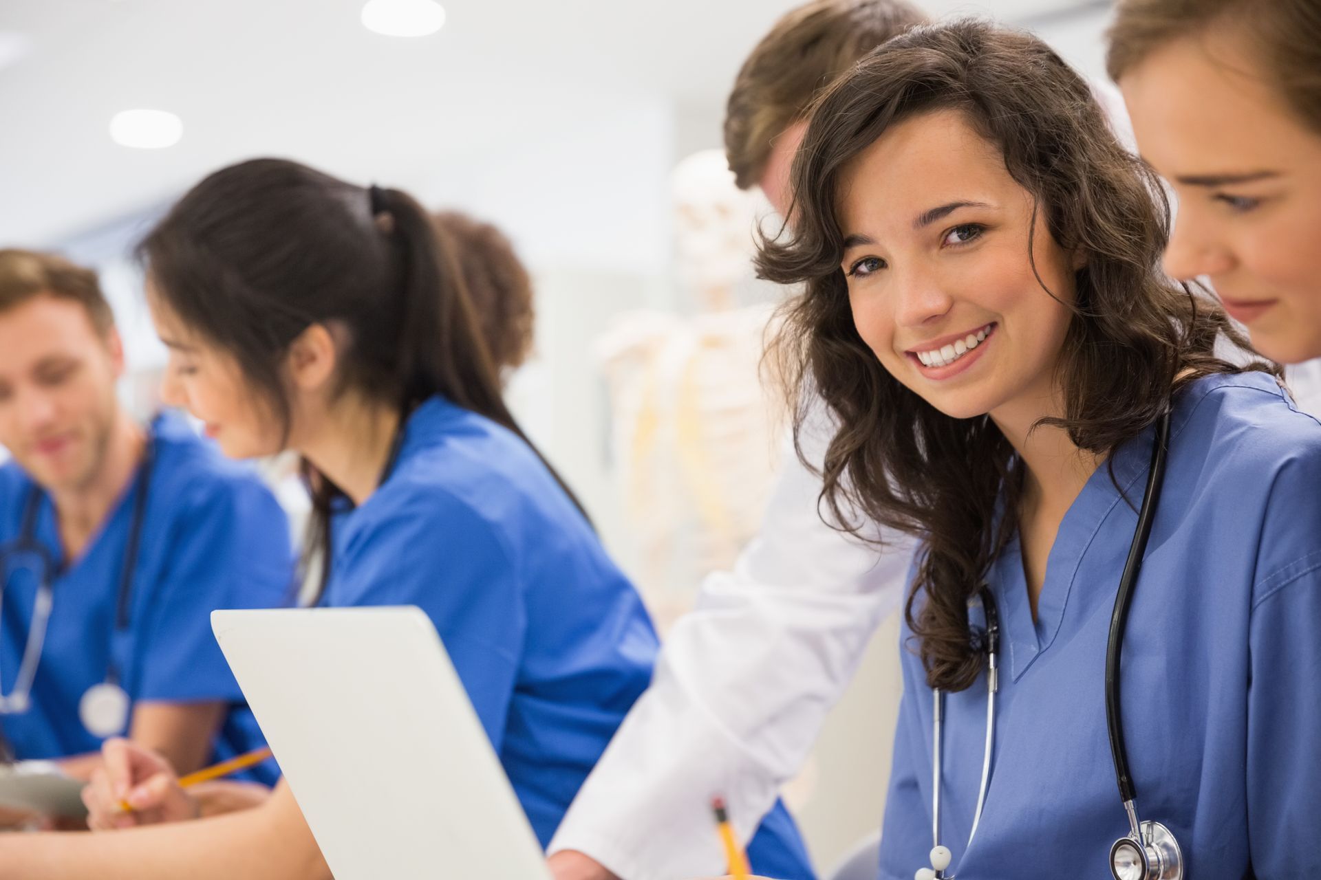 Healthcare trainees working together during a study session with laptops and medical tools visible.