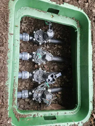 A green box filled with sprinkler valves is sitting on top of a pile of dirt.
